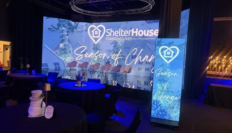 a professional event venue setup for ShelterHouse's "Season of Change" gala, featuring illuminated displays with the…