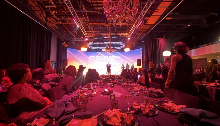 an elegant gala or formal dinner event in a modern venue with dramatic red and pink ambient lighting, featuring guests…