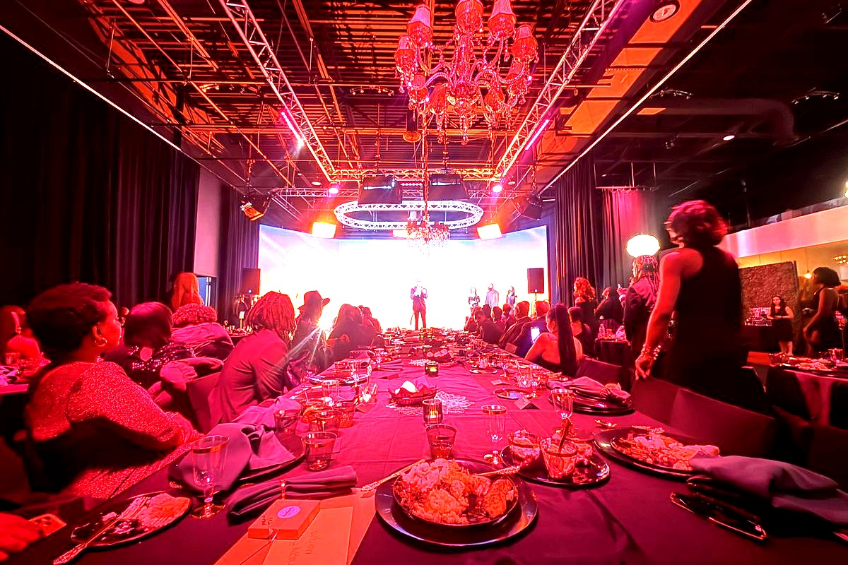 an elegant gala or formal dinner event in a modern venue with dramatic red and pink ambient lighting, featuring guests…