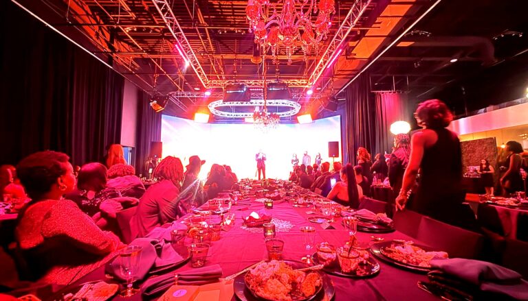 an elegant gala or formal dinner event in a modern venue with dramatic red and pink ambient lighting, featuring guests…