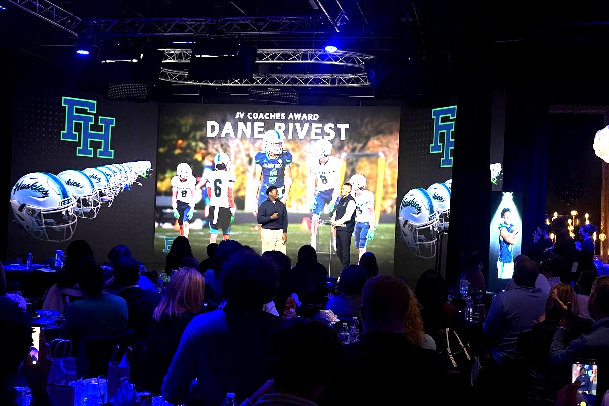 This image captures a JV Coaches Award ceremony honoring Dane Rivest, featuring a large projection screen displaying…