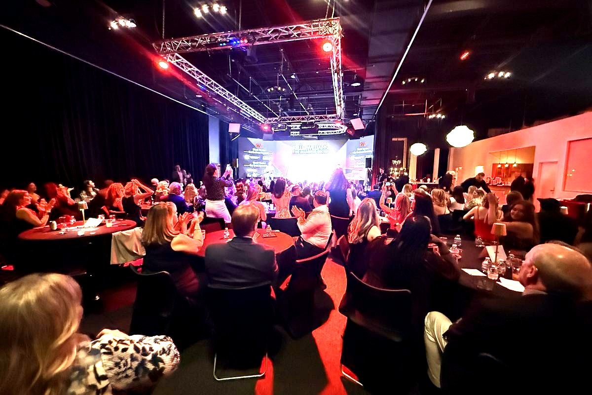 a large corporate gala or conference event with hundreds of attendees seated at round tables in a professionally lit venue…