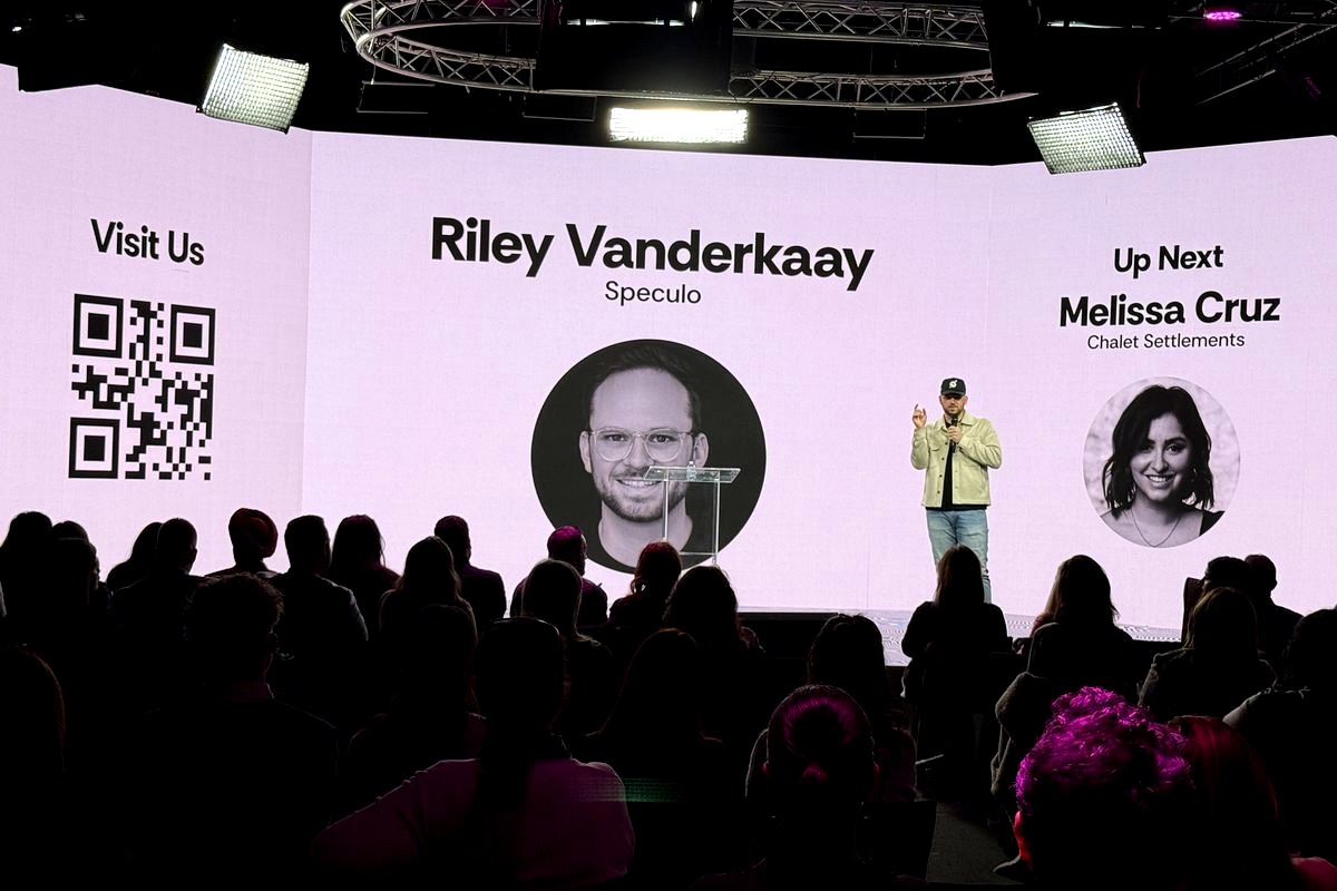 a conference or event stage presentation featuring Riley Vanderkaay from Speculo, with an audience silhouetted in the…