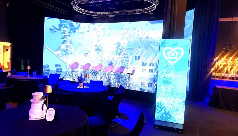 a professional event venue setup for ShelterHouse's "Season of Change" gala, featuring illuminated displays with the…