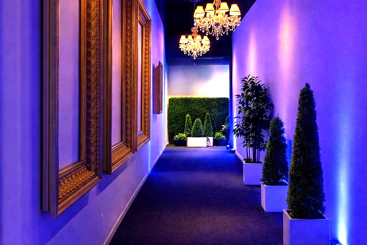 cases an elegant, modern hallway with luxurious chandeliers, ornate gold-framed mirrors, and atmospheric blue uplighting…