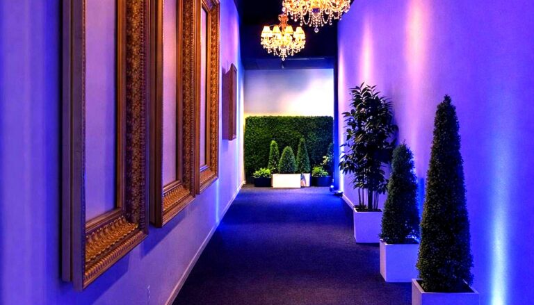 cases an elegant, modern hallway with luxurious chandeliers, ornate gold-framed mirrors, and atmospheric blue uplighting…