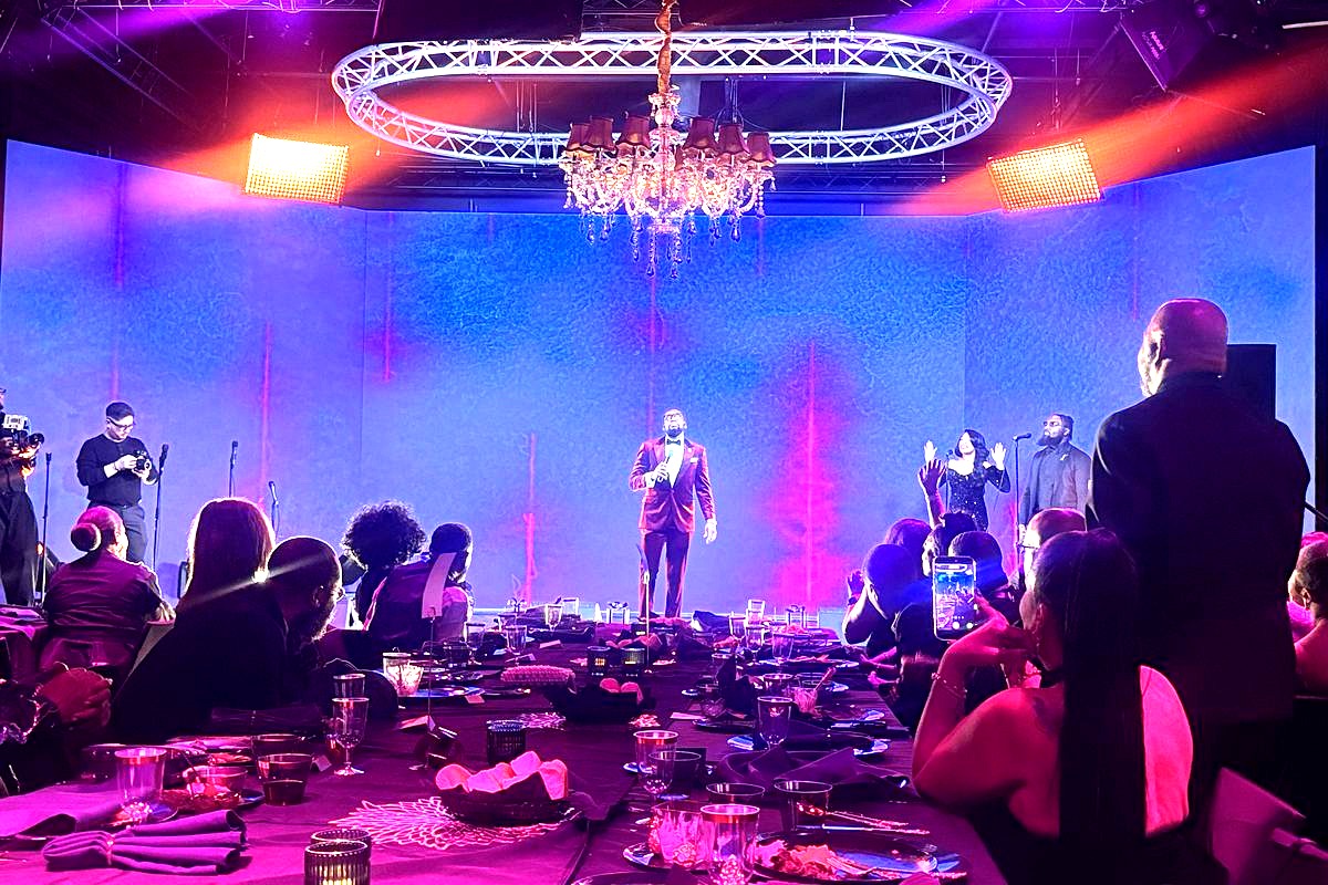 A glamorous indoor gala or formal event features live entertainment on stage with a performer in a burgundy suit…