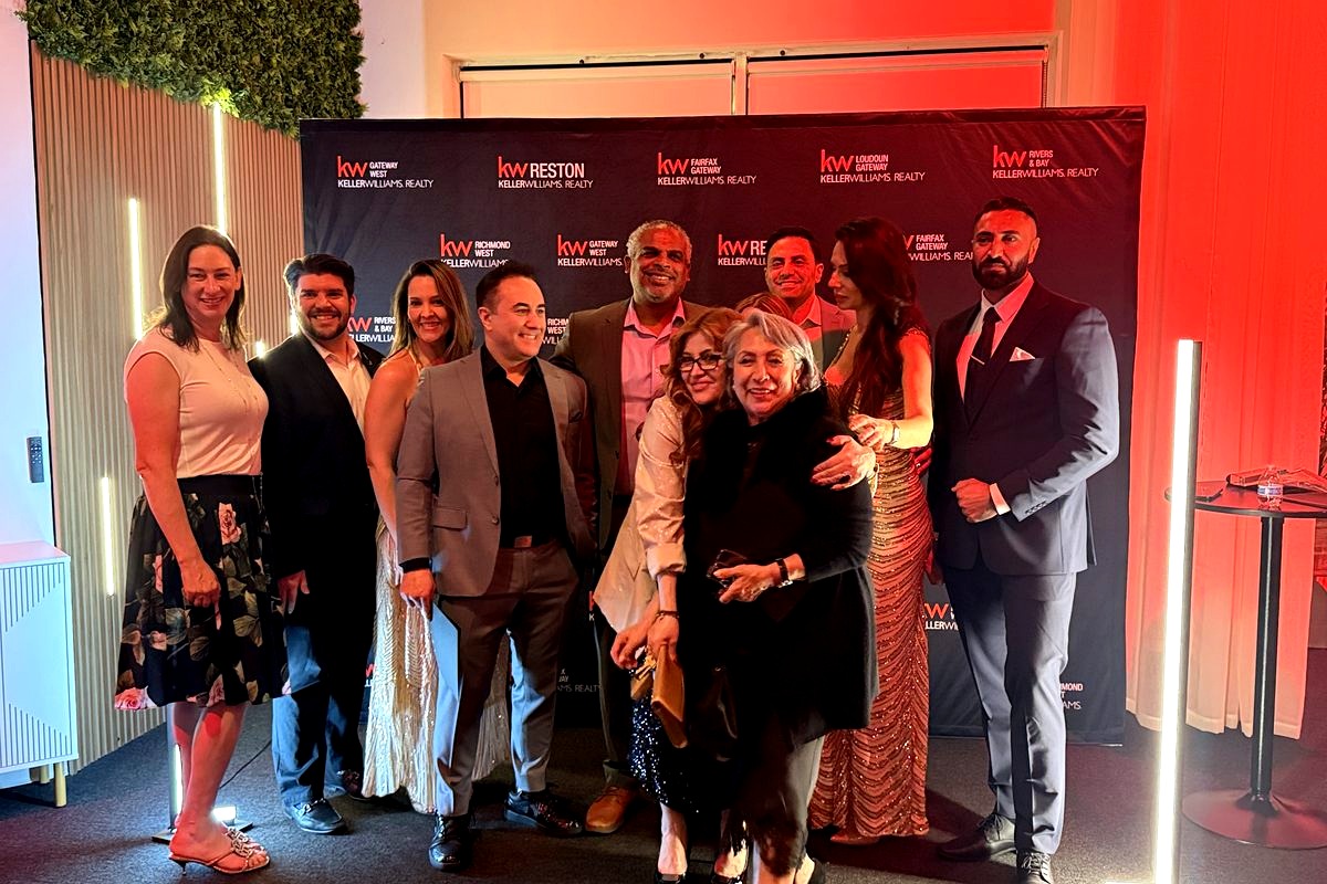 A professional team of real estate agents poses together at a Keller Williams Realty event, smiling in front of branded…
