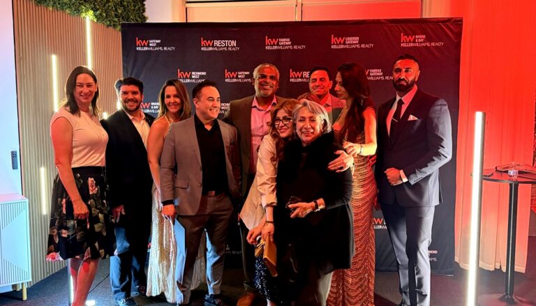 A professional team of real estate agents poses together at a Keller Williams Realty event, smiling in front of branded…