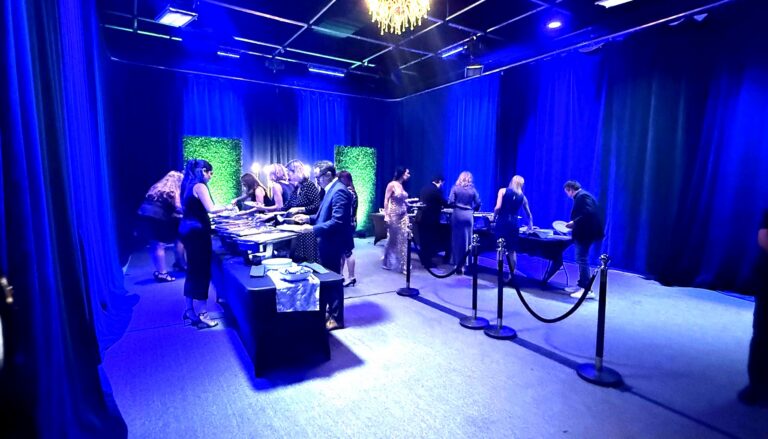 an elegant indoor event or gala taking place in a modern venue with dramatic blue ambient lighting, featuring guests…
