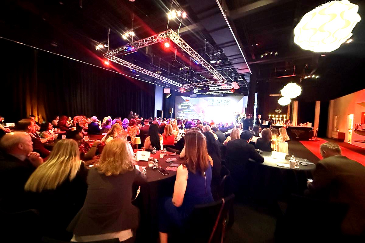 This image captures a formal gala or conference event hosted by Keller Williams, featuring an elegant banquet hall with…