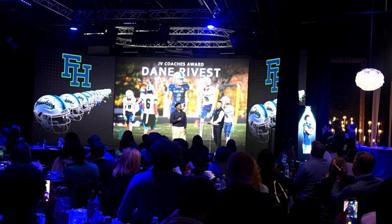 This image captures a JV Coaches Award ceremony honoring Dane Rivest, featuring a large projection screen displaying…