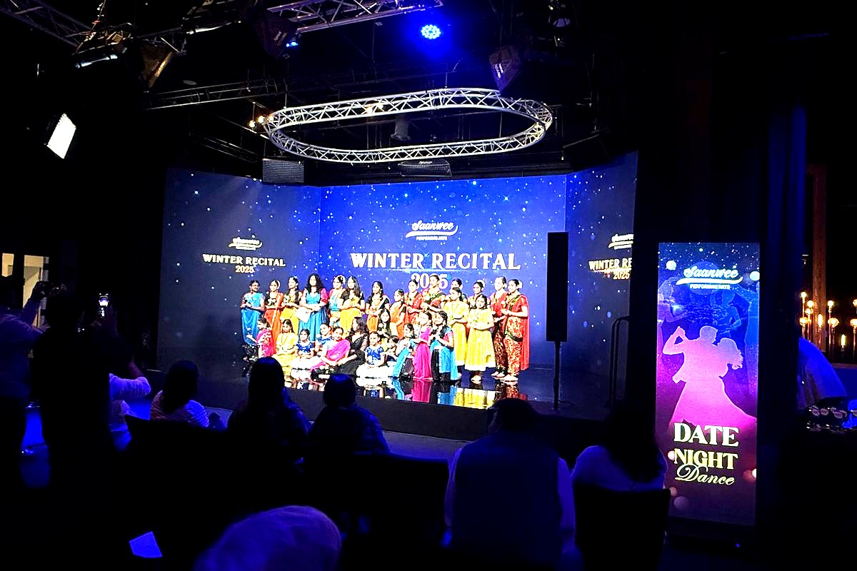 This image captures a Winter Recital 2025 event at the Saanvee performing arts venue, featuring a large group of performers…